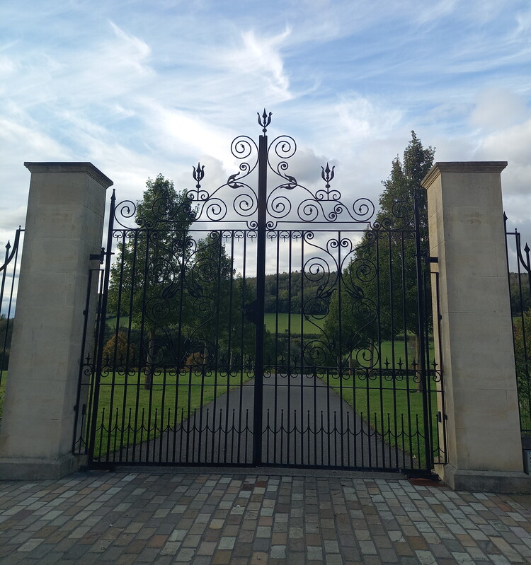 A pair of painted black iron gates in front of a driveway.