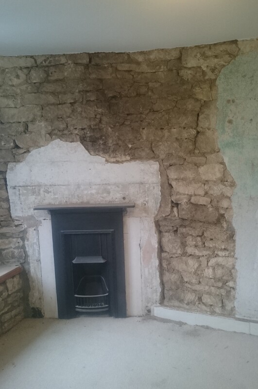 A fireplace set in an unplastered stone wall before work.