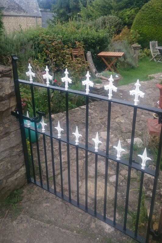 A painted black iron gate with white accents in front of a pathway.